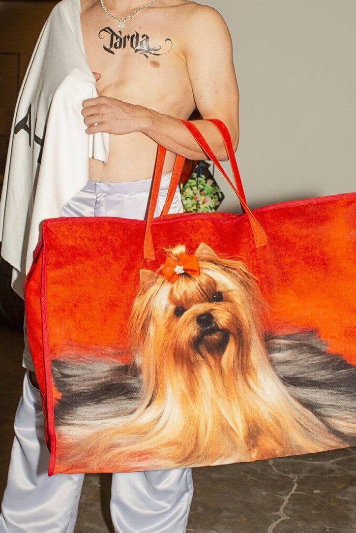 Model carrying a large orange tote printed with a long haired dog