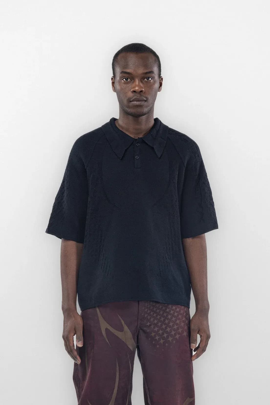 Front view of a dark polo worn with burgundy graphic trousers