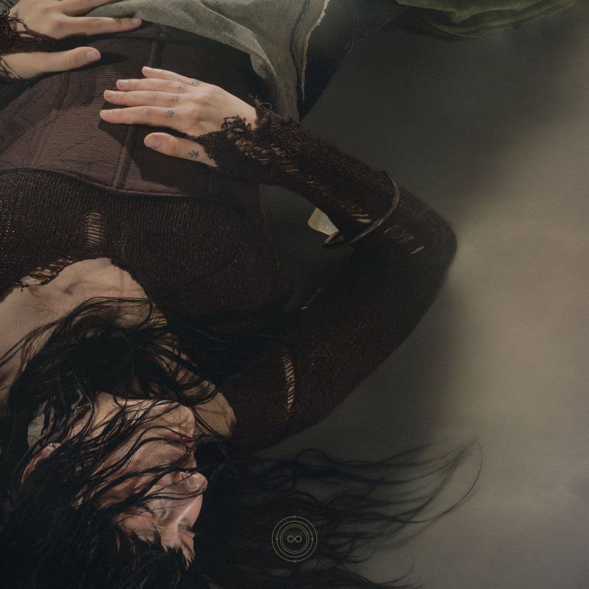 Reclining figure in dark clothing with wet hair and hands resting on the body