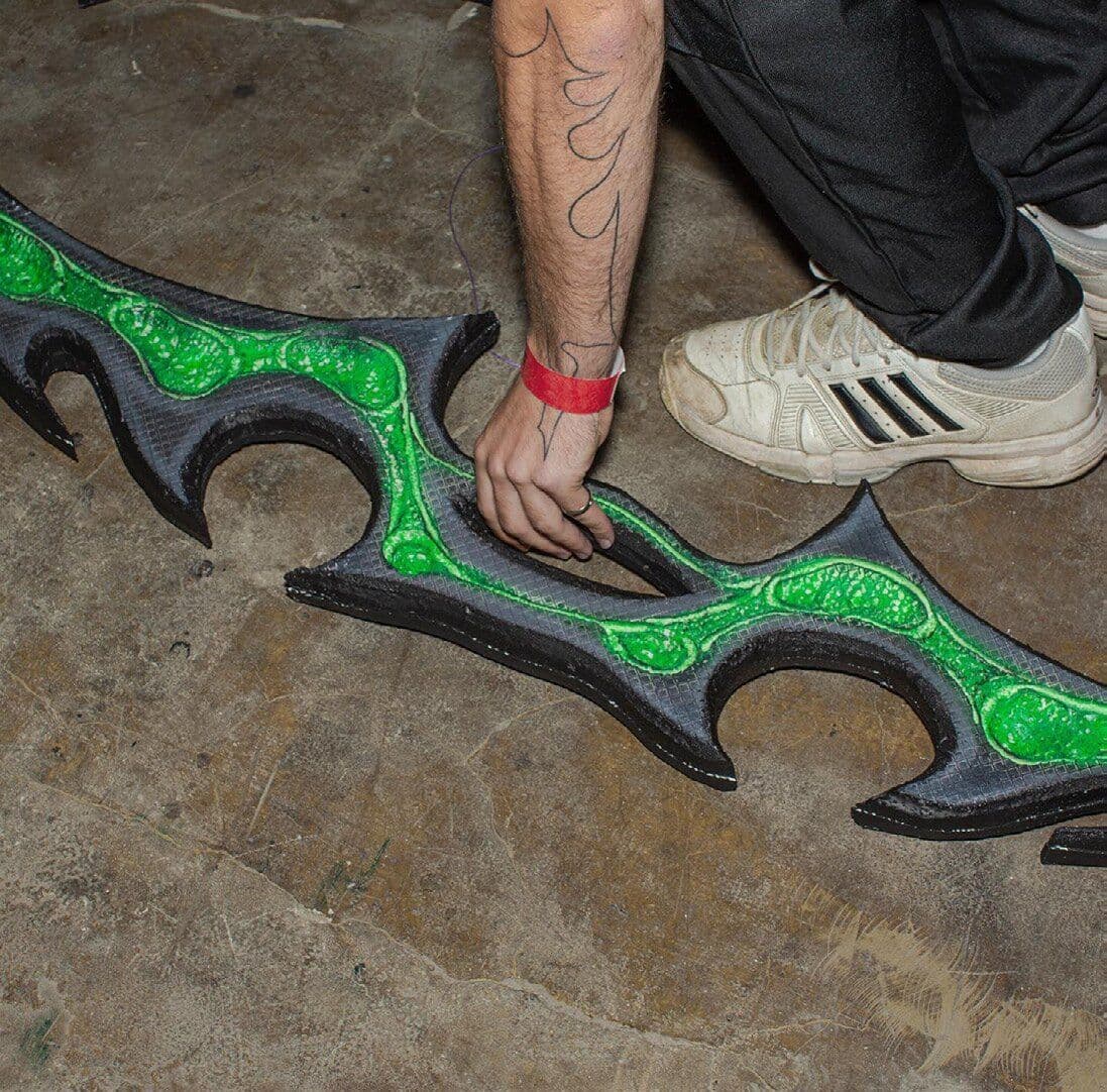 Green and black sculptural accessory beside a hand and white trainer on a stone floor