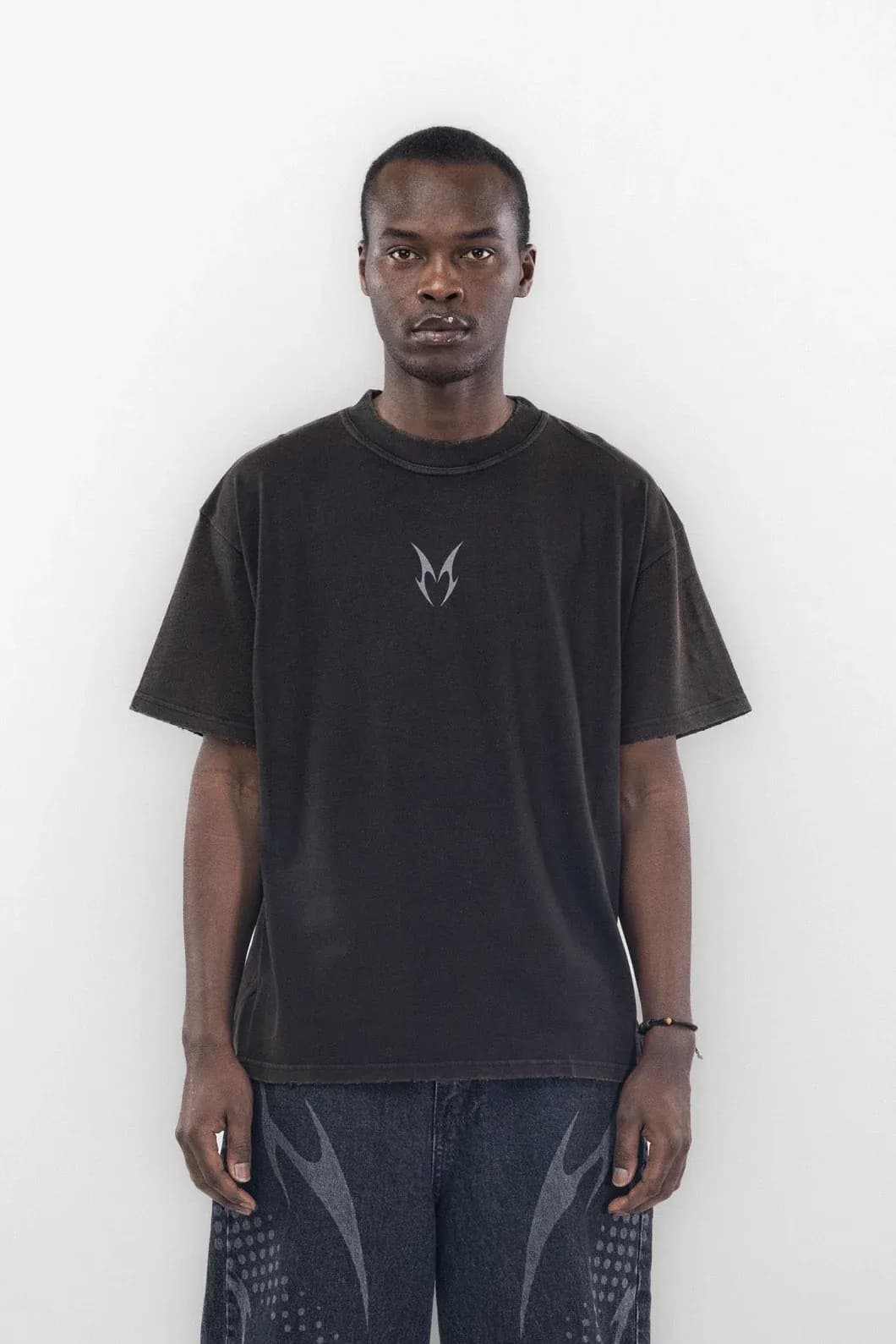 Black T shirt with a small pale chest symbol worn with printed jeans